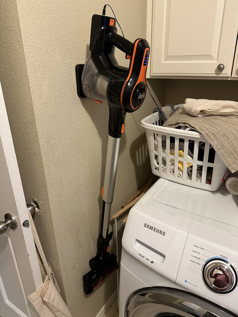 Inse Cordless Vacuum hanging while charging in a laundry room.
