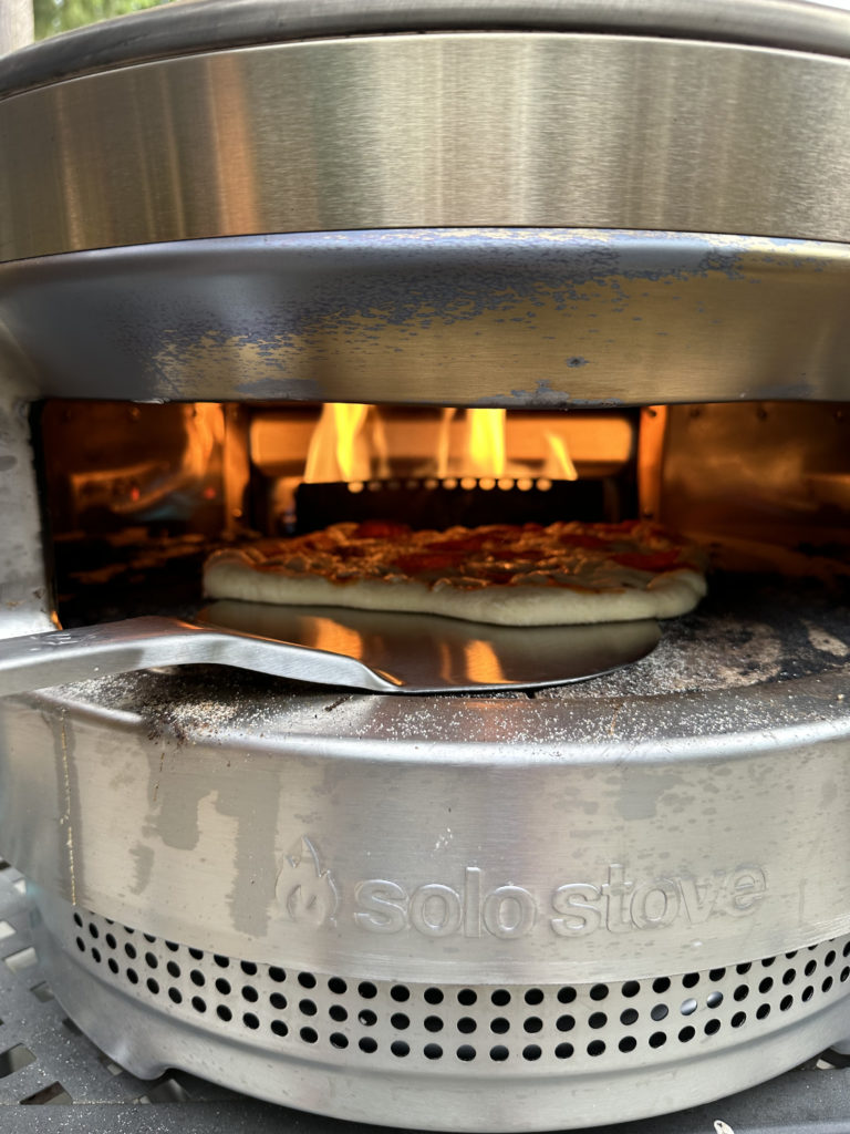 Solo Stove Pizza Oven cooking a homemade pizza using the Solo Stove Stainless Steel peel turner